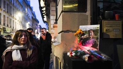 A woman looks on next to tribute flowers and a picture of Emine Kara, one of the victims of a shooting on December 23, 2022, in front of the "Centre democratique du Kurdistan" (Kurdistan democratic centre) in Paris on December 24, 2022. (Photo by Julie SEBADELHA/AFP)
