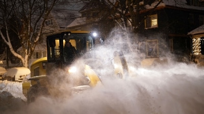 A city worker in a wheel loader clears snow on Norwood Avenue as crews work through the night to reopen the city after a deadly blizzard over the weekend, (AP) A city worker in a wheel loader clears snow on Norwood Avenue as crews work through the night to reopen the city after a deadly blizzard over the weekend, (AP)