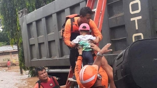 A rescue worker seen holding a child while helping people affected by floods, in Plaridel, Misamis Occidental on December 26. The disaster management council said 1,196 houses were damaged by the floods, while sections of 123 roads and 12 bridges were affected. Some areas continue to remain without power or water supply, AP reported. (Philippine Coast Guard / REUTERS)