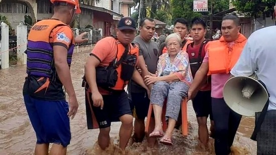 An elderly woman being carried by coast guard personnel as they wade through floodwaters in Plaridel, Misamis Occidental, on December 26. (Philippine Coast Guard / AP)