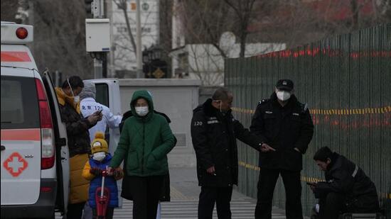 Chinese police personnel check on a man who appears unwell and resting on top of his luggages on the street of Beijing, on Friday. (AP)