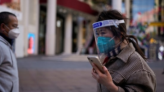 Covid In Shanghai: A woman wearing a protective mask and a face shield walks along in a shopping district in Shanghai, China.(Reuters)