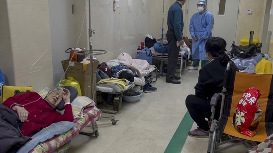 Covid In China: A man talks to a medical worker as elderly patients rest along a corridor of the emergency ward.(AP)