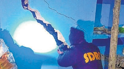An SDRF official inspects the cracks at a house in Joshimath town on Monday. (PTI) An SDRF official inspects the cracks at a house in Joshimath town on Monday. (PTI)