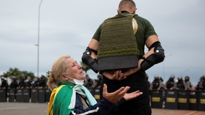 A supporter of Brazil's far-right former President Jair Bolsonaro who along with others disputes the election of leftist President Luiz Inacio Lula da Silva, shields a fellow supporter who prays during protests, in Brasilia. (REUTERS)