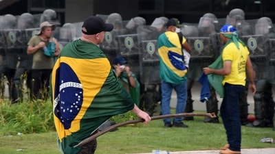 A supporter of Brazilian former President Jair Bolsonaro wrapped in a Brazilian national flag holds a metal bar near soldiers guarding Planalto Presidential Palace in Brasilia . (AFP) A supporter of Brazilian former President Jair Bolsonaro wrapped in a Brazilian national flag holds a metal bar near soldiers guarding Planalto Presidential Palace in Brasilia . (AFP)