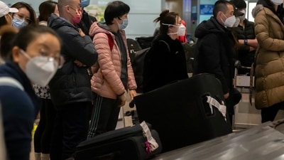 Travelers wearing face masks wait for their luggage in the international arrivals. (AP)