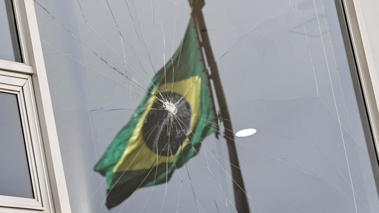 Brazil's flag is reflected on a broken window at Planalto Palace, on January 9. Lula, who took office on January 1 after a bitterly divisive election win over Bolsonaro, returned to work in the pillaged presidential palace where protestors had trashed artwork and offices, shattered windows and doors, and dragged furniture into a reflecting pool. (Ueslei Marcelino / Reuters)