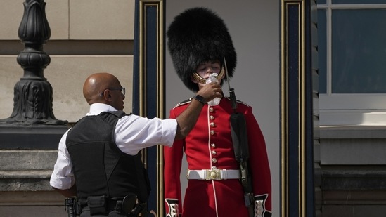 A police officer is seen giving water to a British guard outside Buckingham Palace during a heat wave in London, on July 18, 2022. France, Britain, Spain, and Italy set new average temperature records for 2022, with Europe as a whole enduring its second hottest year ever, Copernicus said (Matt Dunham / AP)