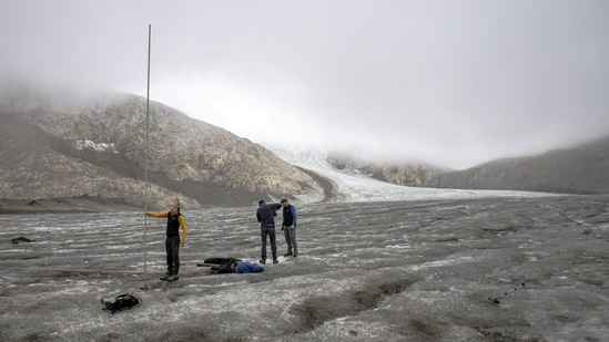 In this file photo from September 2, 2022, members of the Glacier Monitoring in Switzerland (GLAMOS) are seen holding a 6.5-meter-long metal bar that was completely covered by ice in September 2021. They found it lying on the ground in 2022 after the record melting of ice due to the summer heatwave on the Gries Glacier, in Gries, Switzerland.(Denis Balibouse / Reuters)
