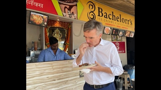 British High Commissioner to India Alex Ellis enjoying Mumbai’s famous snack from a roadside foodstall.(Twitter/@AlexWEllis)