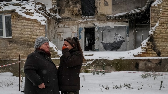 Local residents affected by the ongoing conflict seen near artwork by world-renowned graffiti artist Banksy at the wall of a destroyed building in Horenka, on November 19, 2022. The artist confirmed he was behind seven murals that appeared on destroyed buildings around Kyiv.(Gleb Garanich / REUTERS)