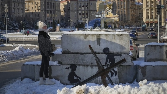A woman stands next to a Banksy artwork in the main square in Kyiv, on December 1, 2022. In the conflict which began in February 2022, both sides have conceded heavy losses, with Moscow desperate to sell any win back home after repeated humiliations and Ukraine determined to hold -- and win back -- ground. (Efrem Lukatsky / AP)