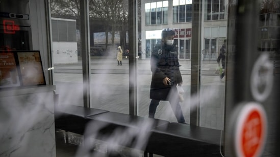Covid In China: A commuter wearing a face mask walks past a closed shop in the central business district in Beijing.(AP)
