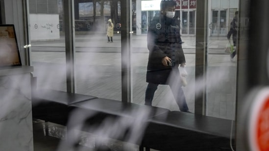 Covid In China: A commuter wearing a face mask walks past a closed shop in the central business district in Beijing.(AP)