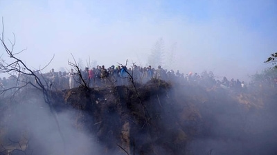 Locals watch the wreckage of the passenger plane in Pokhara, Nepal. The plane was carrying 68 passengers and four crew members. (AP) Locals watch the wreckage of the passenger plane in Pokhara, Nepal. The plane was carrying 68 passengers and four crew members. (AP)