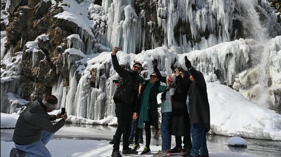 Tourists posing for photographs near a frozen waterfall in the Drang area of Tangmarg, north of Srinagar, Kashmir. (Waseem Andrabi /HT)
