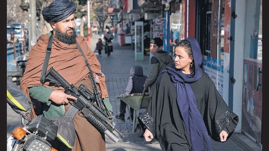 A Taliban fighter stands guard as a woman walks past in Kabul, Afghanistan, on December. 26, 2022 (AP)