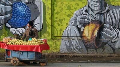 A vendor sells fruits next to a mural wall. (AFP) A vendor sells fruits next to a mural wall. (AFP)