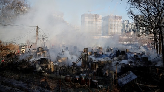 Firefighters work at the scene of a fire at Guryong village, the last slum in the glitzy Gangnam district, as apartment complexes which are currently under construction are seen in the background, in Seoul, South Korea, January 20, 2023. (REUTERS/Kim Hong-Ji)