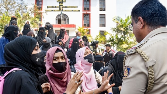 Students wearing burqa and hijab talk to a police officer during their protest, outside the Shivamogga District collector's office, in Shivamogga, February 17, 2022 (PTI)
