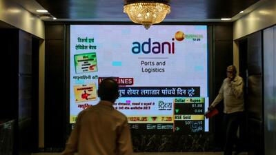 People walk past a screen displaying news featuring on Adani Group inside the BSE building in Mumbai, India, on Thursday. (Bloomberg) People walk past a screen displaying news featuring on Adani Group inside the BSE building in Mumbai, India, on Thursday. (Bloomberg)