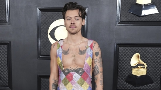 Harry Styles walked the red carpet shirtless in a shimmering sequinned rainbow overall. Harry's sleeveless outfit featured multi-coloured embellishments and showed off the tattoos on his arms and torso. Lastly, Harry rounded it off with a messy hairdo, a sleek gold chain, several gold rings, gold-painted nails, and white-heeled boots.(Jordan Strauss/Invision/AP)