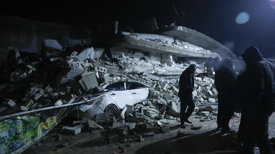 Residents gather in front of the rubble of a building that collapsed, following an earthquake in the village of Azmarin, near the Turkish border in the north of Syria's rebel-held northwestern Idlib province on early Monday.(AFP)