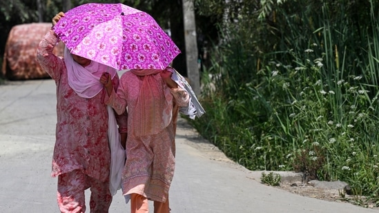 Women hold an umbrella as they walk along a street on a hot summer day in Srinagar. (AFP)