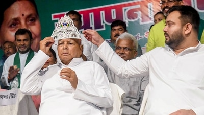 Rashtriya Janata Dal (RJD) chief Lalu Prasad Yadav wears a sliver crown during the party's 28th foundation day, at party office, in Patna on Friday. Leader of Opposition in Bihar Assembly Tejashwi Yadav is also seen. (Pappi Sharma/ANI )