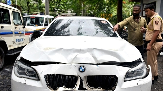 Police personnel inspect a BMW car that ran over two people riding a bike, at Worli Police Station in Mumbai on Sunday. One woman died and one person injured in the accident. (ANI)