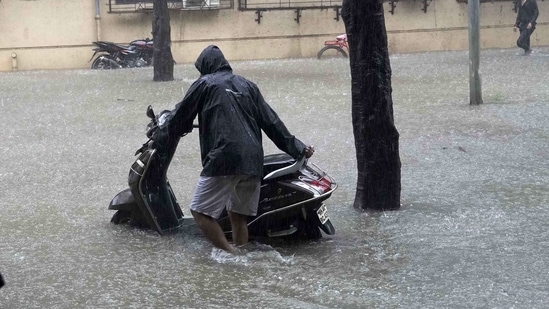 A man wades through a waterlogged road with his scooty at Taloja MIDC in Navi Mumbai. (Bachchan Kumar/ HT PHOTO)