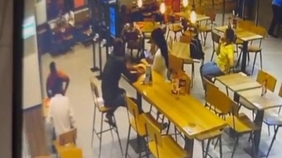 Footage of the incident shows the shooters seated behind the victim, who is sitting across the woman, at a long table. (HT) Footage of the incident shows the shooters seated behind the victim, who is sitting across the woman, at a long table. (HT)