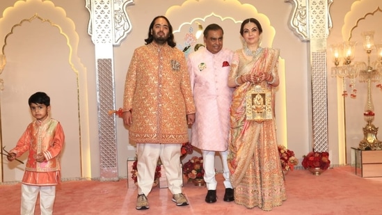 Nita Ambani and Mukesh Ambani pose with groom-to-be Anant Ambani. While Nita Ambani wore a peach silk ghagra that celebrates Indian artisans and cultural legacy, the father of the groom wore a blush pink sherwani. Meanwhile, Anant chose a red and gold sherwani, which he paired with sneakers and a gold elephant brooch. (HT Photo/Varinder Chawla)
