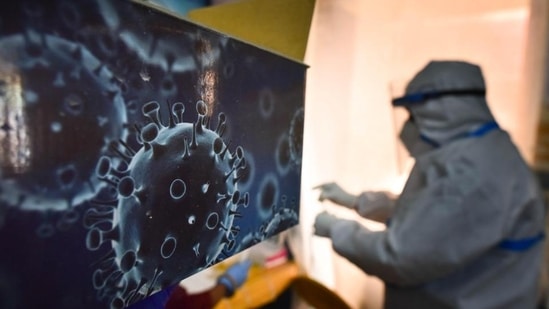 An illustration of the novel coronavirus seen next to a health care worker at a Covid-19 testing centre in New Delhi on October 28. (Sanchit Khanna / HT Photo)