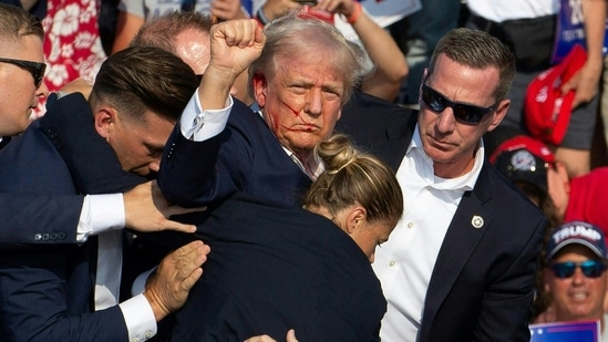 TOPSHOT - Republican candidate Donald Trump is seen with blood on his face surrounded by secret service agents as he is taken off the stage at a campaign event at Butler Farm Show Inc. in Butler, Pennsylvania, July 13, 2024. Donald Trump was hit in the ear in an apparent assassination attempt by a gunman at a campaign rally on Saturday. (Photo by Rebecca DROKE / AFP)