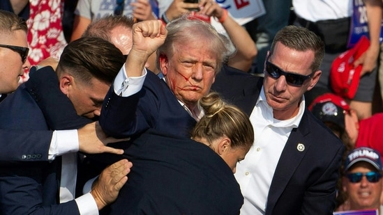 Republican candidate Donald Trump is seen with blood on his face surrounded by Secret Service agents as he is taken off the stage at a campaign event at Butler Farm Show Inc. in Butler, Pennsylvania, July 13, 2024. Donald Trump was hit in the ear in an apparent assassination attempt by a gunman at a campaign rally on Saturday, in a chaotic and shocking incident that will fuel fears of instability ahead of the 2024 US presidential election. (Photo by Rebecca DROKE / AFP)