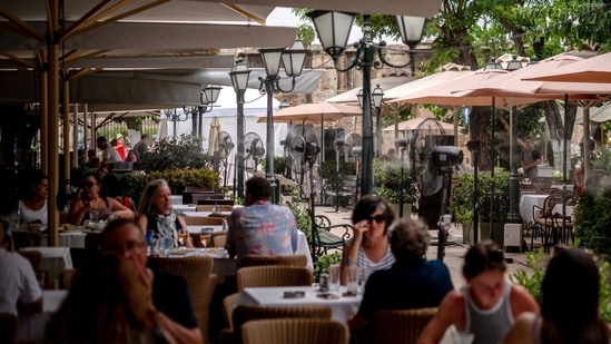 Mist fans cool customers at a restaurant during high temperatures in the Plaka district of Athens, Greece. Domestic tourism falters in Turkey, locals choose affordable tourist destinations in Greece (Photographer: Hilary Swift/Bloomberg)