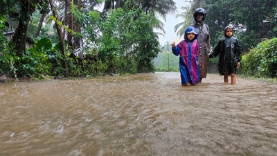 A man along with children walks through a waterlogged street during rains, in Karnataka. (PTI) A man along with children walks through a waterlogged street during rains, in Karnataka. (PTI)