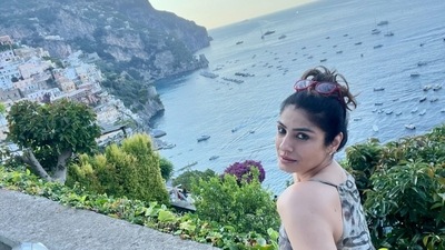 In a photo, Raveena Tandon sat on a wall with the ocean dotted with boats and huge rocks in the background. She was seen in a black and white outfit posing for the camera. In a photo, Raveena Tandon sat on a wall with the ocean dotted with boats and huge rocks in the background. She was seen in a black and white outfit posing for the camera.