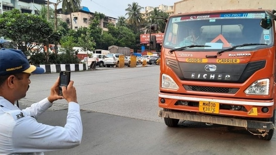 A traffic police personnel seen taking action and issuing e-challan to a heavy vehicle near Mulund Toll Naka. (Praful Gangurde/HT Photo) (HT PHOTO)