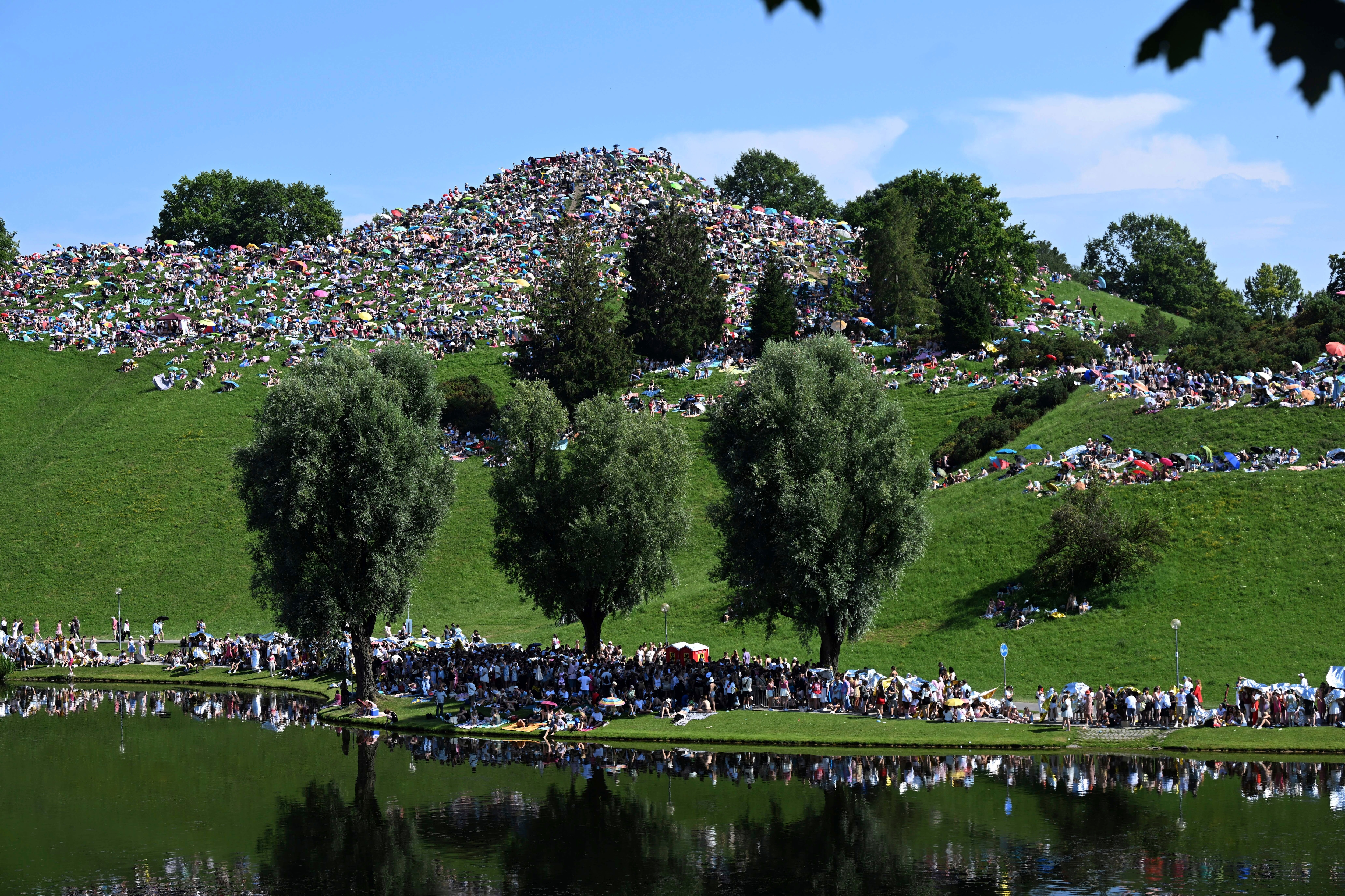 Fans sit on the Olympiaberg in the Olympiapark and wait in the sunshine for the Taylor Swift concert to begin, in Munich, Germany, Sunday July 28, 2024. Taylor Swift's first of two concerts in Munich as part of her "The Eras Tour" is taking place there today. (Felix Hörhager/dpa via AP)