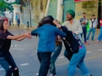 The image shows a woman making a reel while a group of people fight in the background. 