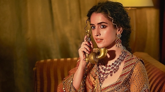 Sanya Malhotra dazzles in a coral-hued lehenga inspired by the forests of Vrindavan, designed by Sunita Rathi. This stunning piece blends art deco with elegant peacock motifs, featuring intricate hand embroidery and appliqué work for modern brides. The ensemble is complemented by jewellery from Gems and Jewels Palace, Jodhpur(Vidhi Godha)