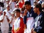 Gold medallist Novak Djokovic of Serbia kisses his medal on the podium next to silver medallist Carlos Alcaraz of Spain and bronze medallist Lorenzo Musetti of Italy