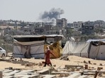 Smoke from Israeli bombardment billows in the background as a woman walks in Khan Yunis in the southern Gaza Strip. (AFP) Smoke from Israeli bombardment billows in the background as a woman walks in Khan Yunis in the southern Gaza Strip. (AFP)