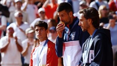 Gold medallist Novak Djokovic of Serbia kisses his medal on the podium next to silver medallist Carlos Alcaraz of Spain and bronze medallist Lorenzo Musetti of Italy (REUTERS)