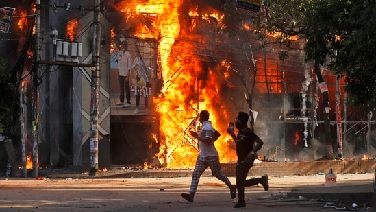 Men run past a shopping center which was set on fire by protesters during a rally against Prime Minister Sheikh Hasina and her government demanding justice for the victims killed in the recent countrywide deadly clashes in Dhaka, on Sunday.(AP)