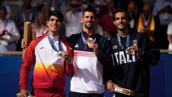 Serbia's Novak Djokovic , center, gold medalist, Spain's Carlos Alcaraz, left, silver medalist, and Italian bronze medalist Lorenzo Musetti pose on the podium,(AP)