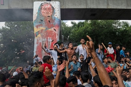Protesters celebrate beside a defaced portrait of Sheikh Hasina in Dhaka after hearing the news of her resignation as PM. (AP) Protesters celebrate beside a defaced portrait of Sheikh Hasina in Dhaka after hearing the news of her resignation as PM. (AP)
